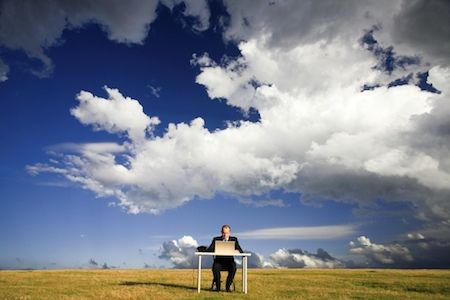 person at a desk in the middle of a field with a big blue sky