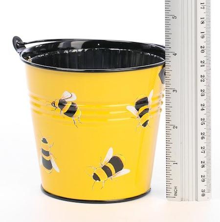 A bucket with bees painted on it next to a ruler